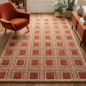 Pode incluir: Um tapete retangular com um padrão geométrico de quadrados em tons de ferrugem e bege. O tapete está colocado sobre um chão de madeira, e uma poltrona cor de ferrugem é visível no fundo. O design do tapete adiciona um toque moderno à sala.