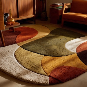May include: A retro-style area rug with an abstract design. The rug features a pattern of overlapping shapes in cream, olive green, mustard yellow, orange, and brown. The rug is made of a soft, plush material, suitable for a living room.