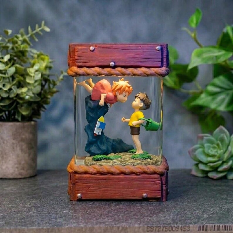 K&ouml;nnte beinhalten: Dekorative Glasbox mit einer Zeichentrickszene mit zwei Figuren. Eine Figur schwebt &uuml;ber einer Felsformation, die andere steht unten und h&auml;lt einen gr&uuml;nen Eimer. Die Box hat einen Holzrahmen mit Seildetails.