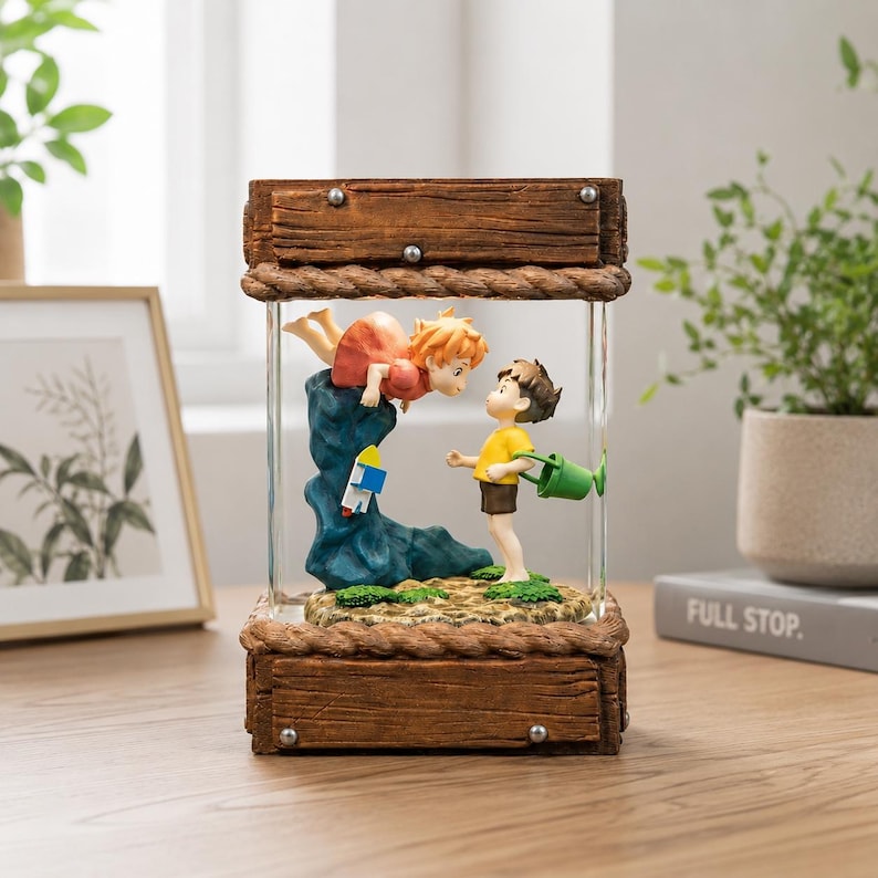 K&ouml;nnte beinhalten: Eine dekorative Glasbox zeigt eine Szene mit zwei animierten Figuren, eine in einem roten Kleid und die andere in einem gelben Hemd, mit einer blauen Felsformation und einer kleinen Rakete. Die Box hat einen Holzrahmen.
