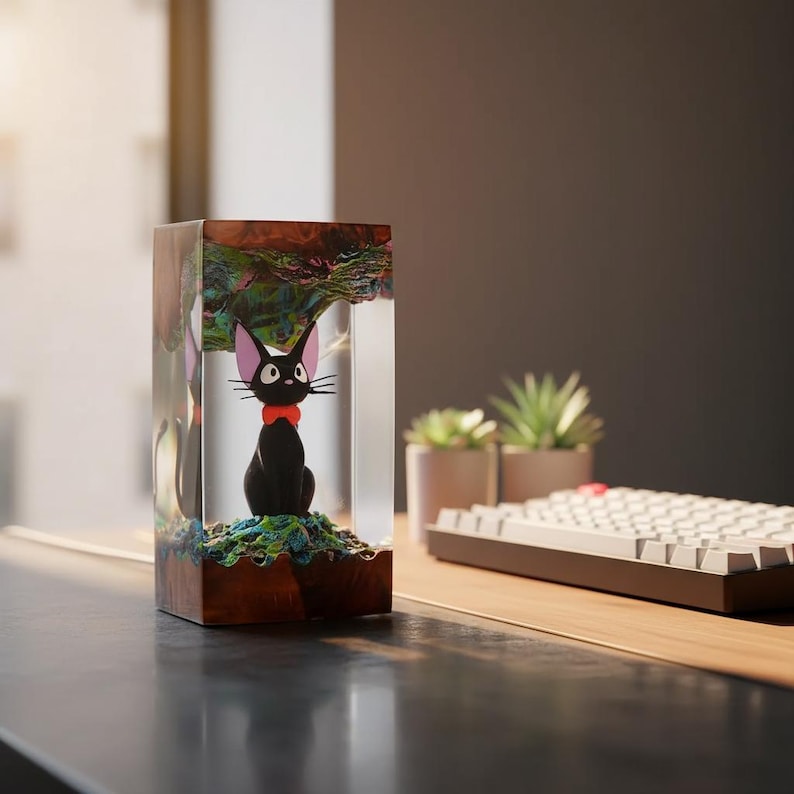 May include: A black cat figurine with a red bow is encased in a clear resin block. The base is a dark wood, and the top has a colorful, textured design. The cat is sitting on a green and blue base. A unique decorative item.