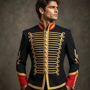 May include: A black military-style jacket featuring a high collar, red cuffs, and gold braided cord detailing across the front. The garment includes gold-toned buttons down the centre and embroidered gold leaf patterns on the sleeves and collar.