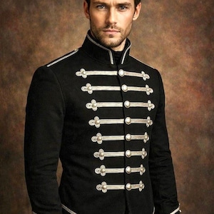 Puede incluir: Una chaqueta negra de estilo militar con cuello alto, mangas largas y adornos metálicos plateados. La parte delantera está decorada con cordones trenzados plateados horizontales y botones plateados redondos dispuestos en pares.