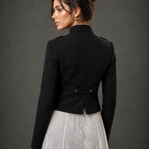 May include: A black jacket with a high collar and button details. The jacket has a tailored fit and is paired with a white lace skirt. The image is set against a dark gray background.