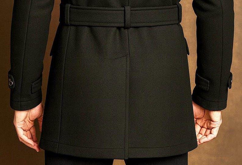 May include: A black coat featuring a belted waist with a matching fabric belt, long sleeves with buttoned cuff tabs, and a central vertical seam detail on the back. The coat has a structured fit and reaches mid-thigh length, showcasing clean lines.