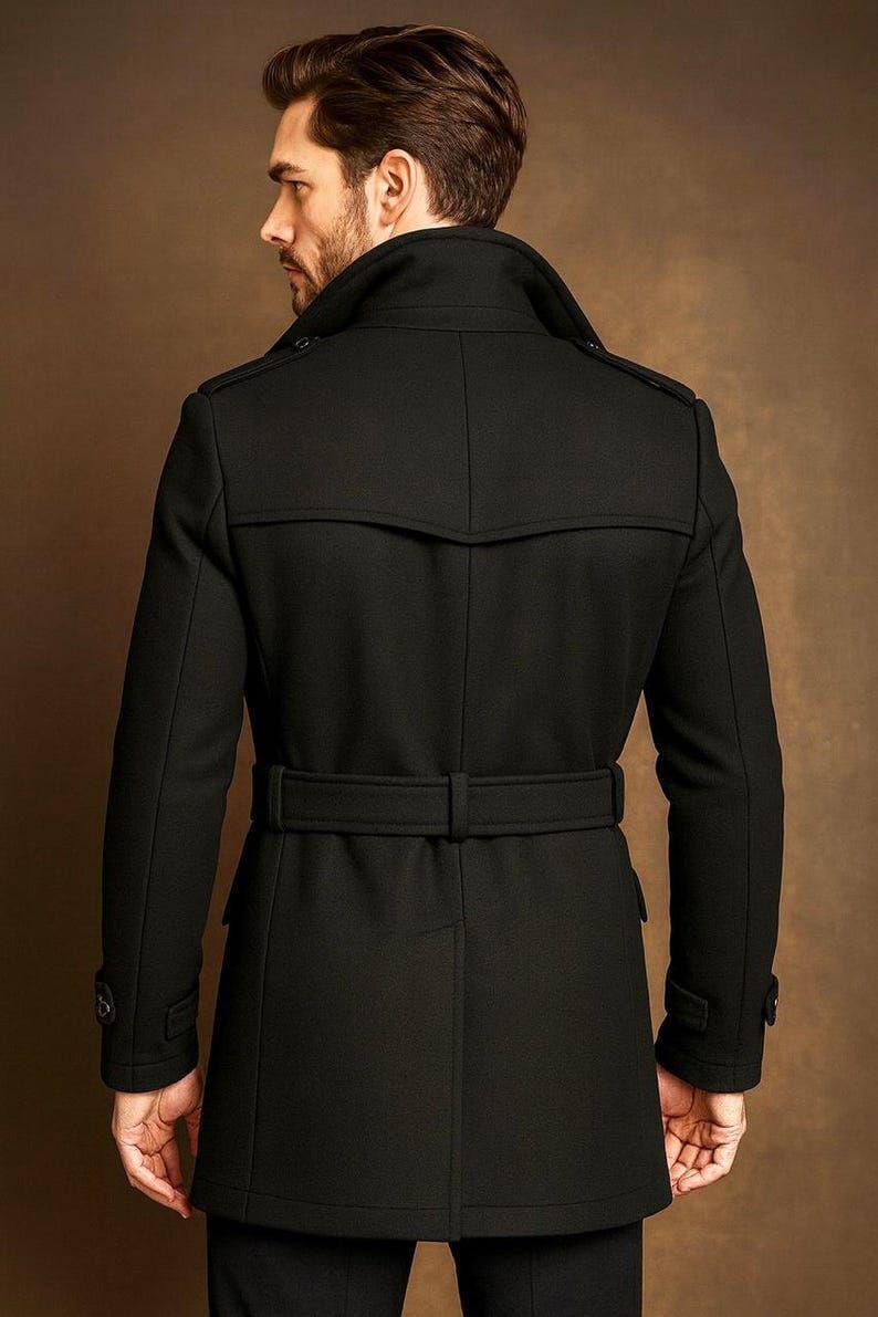 May include: A black trench coat featuring a wide collar, shoulder epaulets, and a matching waist belt with a buckle. The coat has long sleeves with buttoned cuffs, a back yoke, and a central vent at the hem, providing a structured silhouette.