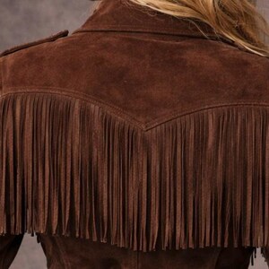 May include: A brown suede jacket with fringe detailing on the sleeves and back. The jacket has a classic western style with a collar and shoulder accents. The fringe adds a decorative element to the garment.