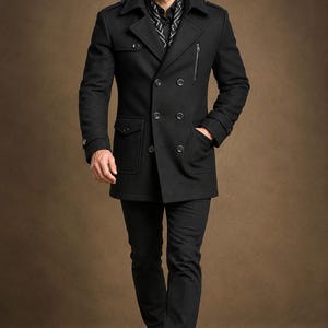 May include: A black double-breasted pea coat featuring a wide collar, shoulder epaulets, and a vertical zippered chest pocket. The coat includes two large flap pockets at the waist, black buttons, and is worn over a black shirt with a white pattern.