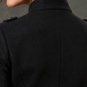 May include: Close-up of the back of a black coat. The coat has a high collar and two small decorative buttons on each shoulder. The fabric appears to be a smooth, woven material.