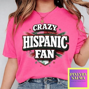May include: A bright pink t-shirt with the words "CRAZY HISPANIC FAN" in a bold, layered design. The text is white with black and green accents, set against a starburst and star background. The shirt is a vibrant, eye-catching piece.