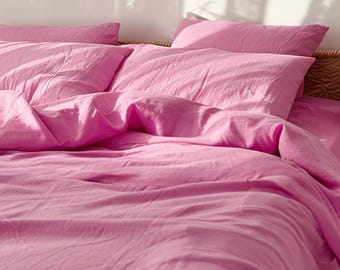 May include: A bed with pink bedding, including a duvet cover and two pillows. The bedding is a solid, vibrant pink color. The pillows are rectangular and placed on the bed. The bed frame is partially visible, with a woven texture.