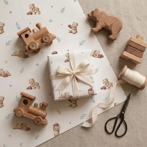 May include: A selection of wooden toys and gift wrapping items. The image features a wooden bear, two toy trains, a wrapped gift with a cream bow, and wrapping paper printed with teddy bears and cars. Scissors and a spool of ribbon are also visible.