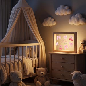 Pode incluir: Uma caixa de luz retangular com moldura de madeira exibe uma estampa rosa de la&ccedil;os e cerejas com o nome "Claudia Alves" no centro. O letreiro iluminado est&aacute; sobre uma c&ocirc;moda de madeira ao lado de um urso de pel&uacute;cia e uma ovelha de pel&uacute;cia.
