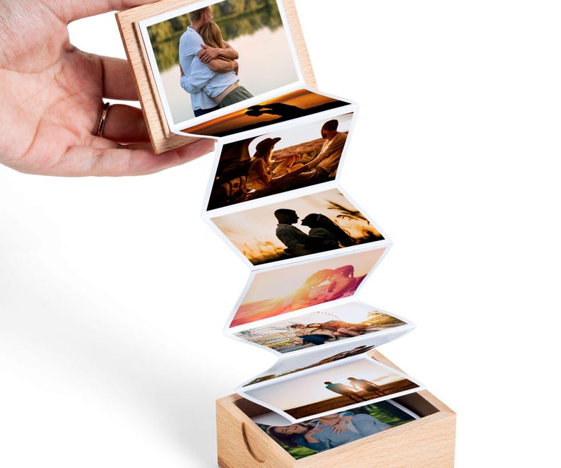 May include: A wooden photo box with a series of attached photos, each displaying a different image. The photos are in a zig-zag pattern, with the top photo held in place by a wooden frame. The images depict couples in various outdoor settings.
