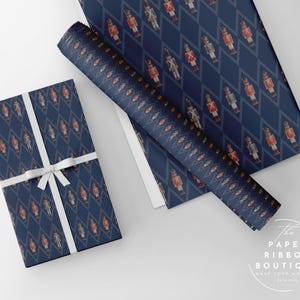 May include: Dark blue wrapping paper featuring a repeating diamond pattern with small nutcracker figures in red and white uniforms. One rectangular gift is wrapped in the paper and tied with a white ribbon. The text The Paper Ribbon Boutique is visible.