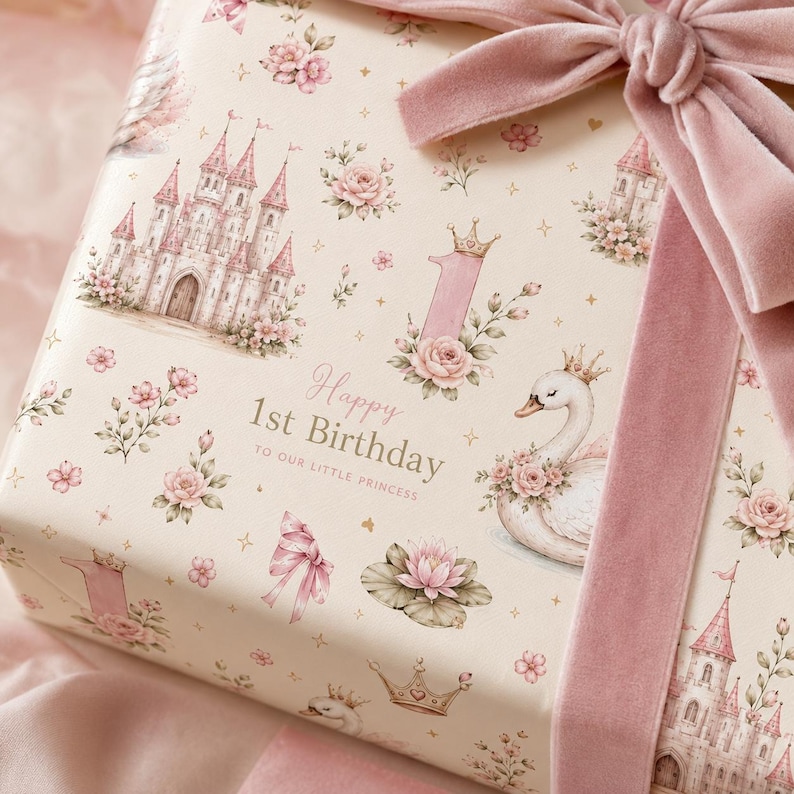 May include: A gift wrapped in cream-colored paper featuring a pattern of pink castles, swans with crowns, lotus flowers, and the number one. The text reads Happy 1st Birthday TO OUR LITTLE PRINCESS. A wide, dusty pink velvet ribbon is tied in a bow.