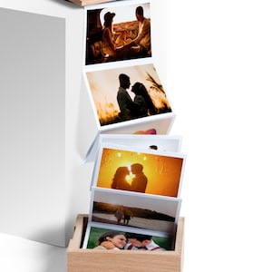 May include: A wooden photo box with a series of printed photographs. The photos depict couples in various outdoor settings. The box is light brown, and the photos are arranged in a cascading manner.