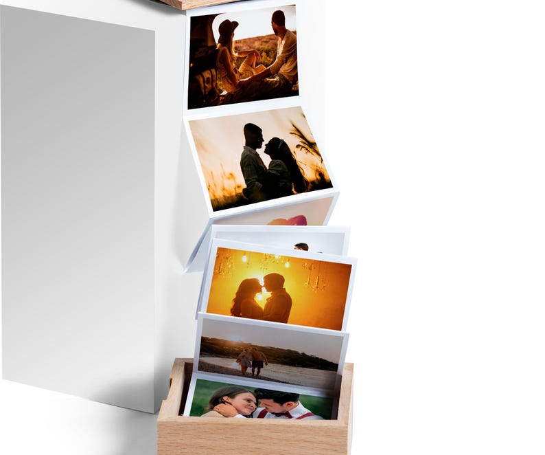 May include: A wooden photo box with a series of printed photographs. The photos depict couples in various outdoor settings. The box is light brown, and the photos are arranged in a cascading manner.
