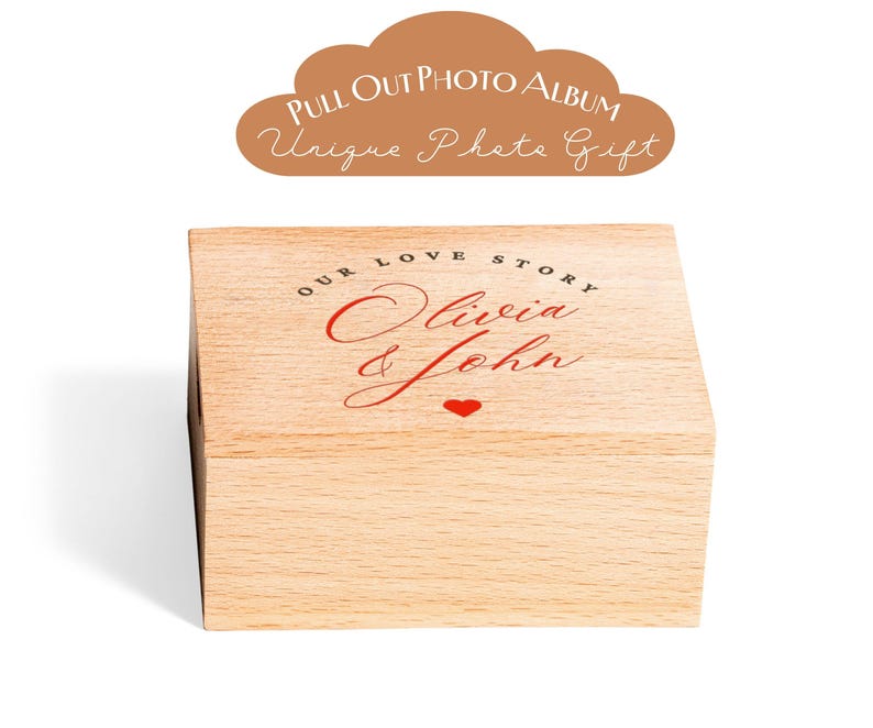 May include: A wooden photo album box with the words "Our Love Story Olivia & John" in red script, and a small red heart. The box is light-colored wood and has a pull-out design. Above the box is a brown cloud-shaped graphic with the text "Pull Out Photo Album Unique Photo Gift."