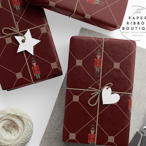 Puede incluir: Regalos envueltos con un fondo burdeos y un patrón repetido de soldaditos de juguete. Cada paquete está atado con hilo y una etiqueta blanca. El logotipo de The Paper Ribbon Boutique es visible.