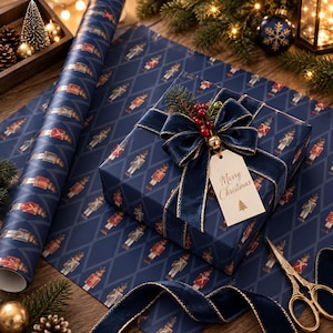 May include: A square gift box wrapped in dark blue paper with a repeating nutcracker pattern, tied with a navy velvet ribbon, a gold bell, red berries, and a beige gift tag with the text Merry Christmas and a small pine tree icon.