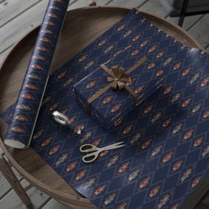 May include: A roll of navy blue wrapping paper featuring a repeating diamond pattern with small nutcracker figures, a gift box wrapped in the same paper with a brown ribbon, a small roll of clear tape, and silver metal scissors.