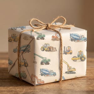 Puede incluir: Una caja de regalo envuelta en papel beige con un patrón repetido de vehículos de construcción de colores. La caja está atada con cuerda.