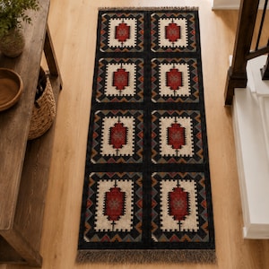 Top view of dark charcoal tribal area rug with repeating square medallion motifs in multicolor, handmade flatweave wool jute rug with fringe