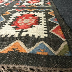 Handmade black southwestern area rug with bold geometric pattern in multicolor rust ivory teal and orange, eco friendly wool jute flatweave
