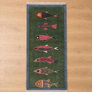 Könnte beinhalten: Ein rechteckiger Teppich mit dunkelgrünem Hintergrund und sieben verschiedenen Fischmotiven, die in einer vertikalen Reihe angeordnet sind. Jeder Fisch zeigt ein einzigartiges Muster und eine Farbkombination aus Orange, Pink, Blau und Beige. Der Teppich hat eine blau-weiße geometrische Bordüre und weiße Fransen an den oberen und unteren Kanten.