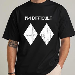 May include: Black t-shirt featuring the white text "I'M DIFFICULT" above two white diamond shapes. The shirt has a crew neck and short sleeves.