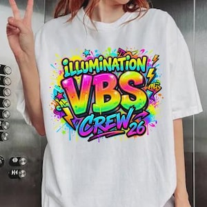 May include: White t-shirt with a colorful graphic design. The design features the words "ILLUMINATION VBS CREW 26" in vibrant rainbow colors, surrounded by stars, lightning bolts, and graffiti-style accents. The shirt is a casual, unisex style.