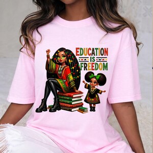 May include: Pink t-shirt with a graphic featuring two Black girls, one seated on books labeled "Black History" and the other standing. The text "EDUCATION IS FREEDOM" is above the girls.