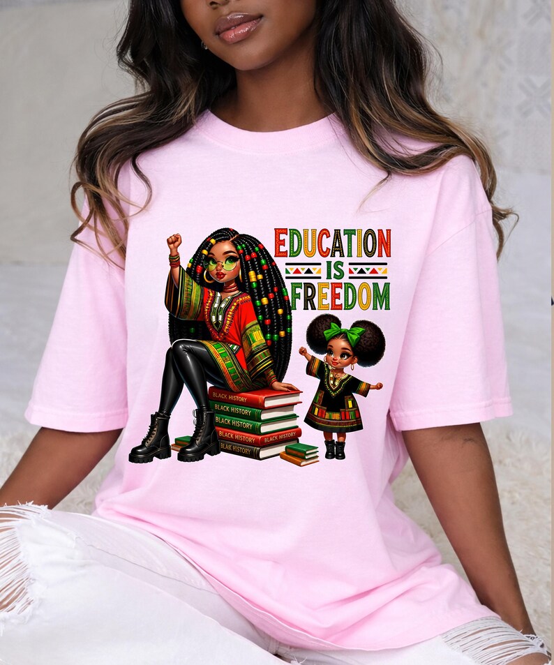 May include: Pink t-shirt with a graphic featuring two Black girls, one seated on books labeled "Black History" and the other standing. The text "EDUCATION IS FREEDOM" is above the girls.