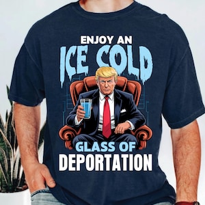 May include: Navy blue t-shirt featuring a graphic of a man in a suit holding a glass of water, seated in a chair. The text reads "ENJOY AN ICE COLD GLASS OF DEPORTATION" in white and light blue.
