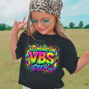 May include: A black t-shirt with the words "ILLUMINATION VBS CREW 26" in a colorful, graffiti-style design. The shirt is worn by a person wearing a leopard print headscarf and aviator sunglasses.