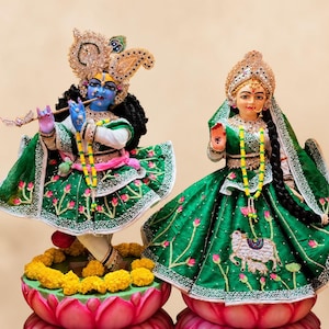 May include: Two ornate statues of deities. One is blue-skinned, playing a flute, wearing a jeweled crown and green dress. The other is fair-skinned, with a jeweled crown and green dress. Both stand on lotus flower bases.