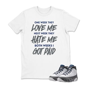 May include: White t-shirt with the text "ONE WEEK THEY LOVE ME NEXT WEEK THEY HATE ME BOTH WEEKS I GOT PAID" in dark gray. A pair of white and gray sneakers with black accents are at the bottom.