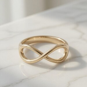 May include: A polished gold ring featuring a continuous infinity symbol design. The band is crafted from a smooth, reflective yellow metal, forming a symmetrical loop that represents the mathematical infinity sign in a simple, solid construction.