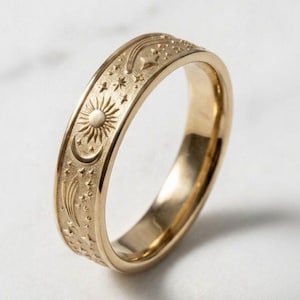 May include: A gold-colored ring with celestial engravings. The ring features a sun, crescent moon, stars, and shooting stars design. The ring is a band style and has a polished finish.