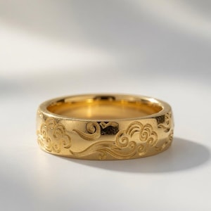Könnte beinhalten: Ein polierter Goldring mit einem eingravierten Muster aus wirbelnden Wolken und Windmotiven, das sich um die gesamte Außenfläche zieht. Das Metall hat eine reflektierende Oberfläche, die die feinen, vertieften Linien des Designs betont.