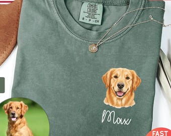 May include: A moss green Comfort Colors t-shirt with a golden retriever graphic and the name "Max". The shirt has a crew neck and short sleeves. A silver necklace with a pendant is also visible. The shirt is a size S-CH.
