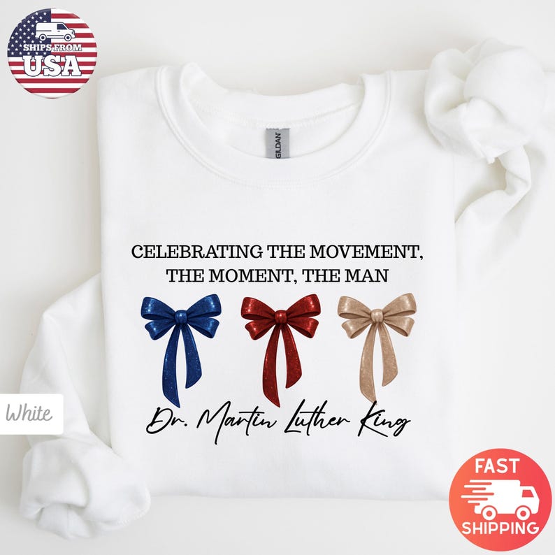 Peut inclure: Sweat-shirt blanc avec l'inscription "CELEBRATING THE MOVEMENT, THE MOMENT, THE MAN" et "Dr. Martin Luther King". Le motif comprend des n&oelig;uds bleus, rouges et dor&eacute;s. Le sweat-shirt a un col rond.