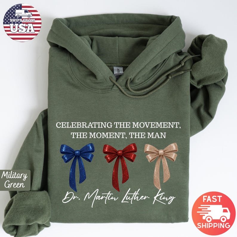 Peut inclure: Sweat &agrave; capuche vert militaire avec le texte "CELEBRATING THE MOVEMENT, THE MOMENT, THE MAN" et "Dr. Martin Luther King". Le motif comprend trois n&oelig;uds d&eacute;coratifs bleus, rouges et beiges.