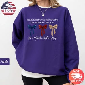 Peut inclure: Un sweat-shirt violet avec le texte "CELEBRATING THE MOVEMENT, THE MOMENT, THE MAN" et "Dr. Martin Luther King." Le design comprend trois n&oelig;uds papillon bleus, rouges et dor&eacute;s. Le sweat-shirt a un col rond.