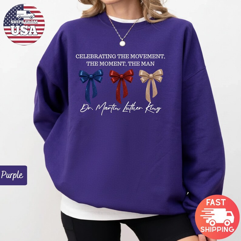 Peut inclure: Un sweat-shirt violet avec le texte "CELEBRATING THE MOVEMENT, THE MOMENT, THE MAN" et "Dr. Martin Luther King." Le design comprend trois n&oelig;uds papillon bleus, rouges et dor&eacute;s. Le sweat-shirt a un col rond.