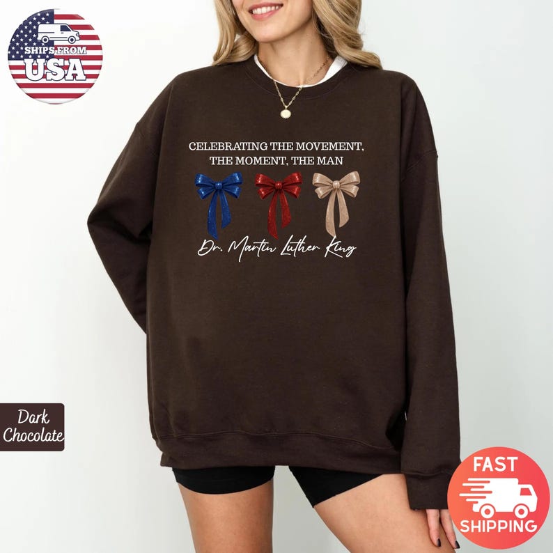 Peut inclure: Sweat-shirt marron fonc&eacute; avec l'inscription "CELEBRATING THE MOVEMENT, THE MOMENT, THE MAN" et "Dr. Martin Luther King." Le motif comprend trois n&oelig;uds papillon bleus, rouges et beiges. Le sweat-shirt a un col blanc.