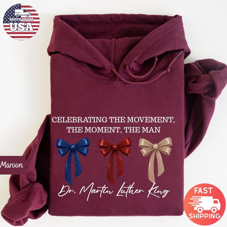 Peut inclure: Sweat &agrave; capuche bordeaux avec le texte "CELEBRATING THE MOVEMENT, THE MOMENT, THE MAN" et "Dr. Martin Luther King." Comporte trois n&oelig;uds d&eacute;coratifs bleus, rouges et dor&eacute;s. Le sweat &agrave; capuche est pli&eacute;.