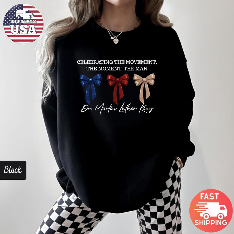 Peut inclure: Sweat-shirt noir avec le texte "CELEBRATING THE MOVEMENT, THE MOMENT, THE MAN" et "Dr. Martin Luther King". Comporte trois graphiques de n&oelig;uds papillon bleus, rouges et beiges. Le sweat-shirt est de style col rond.