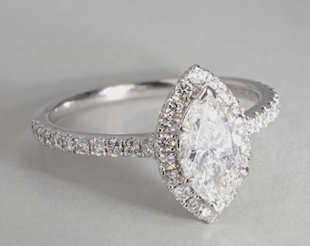 May include: A silver-toned ring featuring a central marquise-cut stone surrounded by a halo of smaller round stones. The band is also encrusted with small round stones. The text FAUX JEWEL is visible on the side of the ring band.